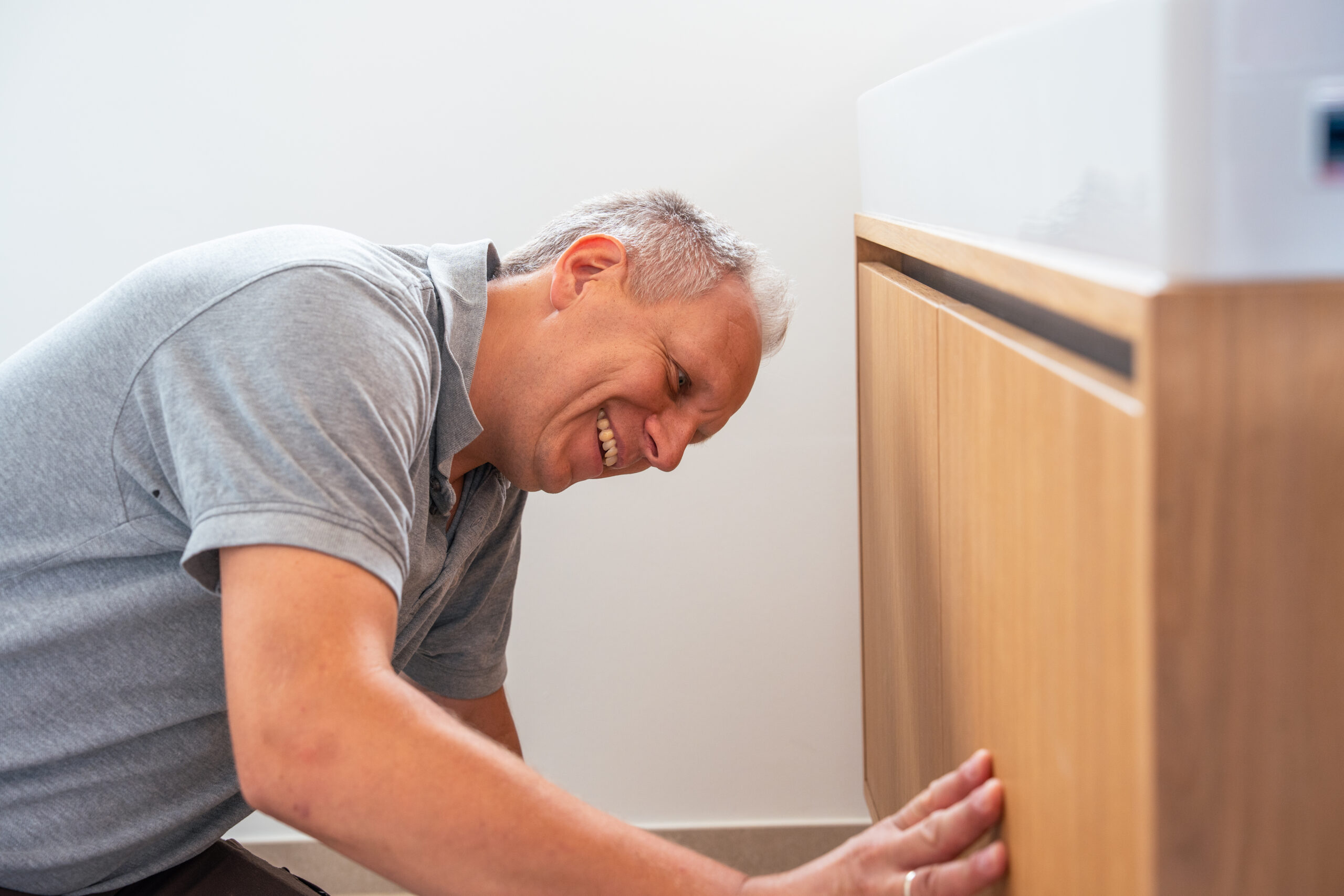 Tischlermeister lächelt, während er einen Holzschrank unter einem Waschbecken montiert.