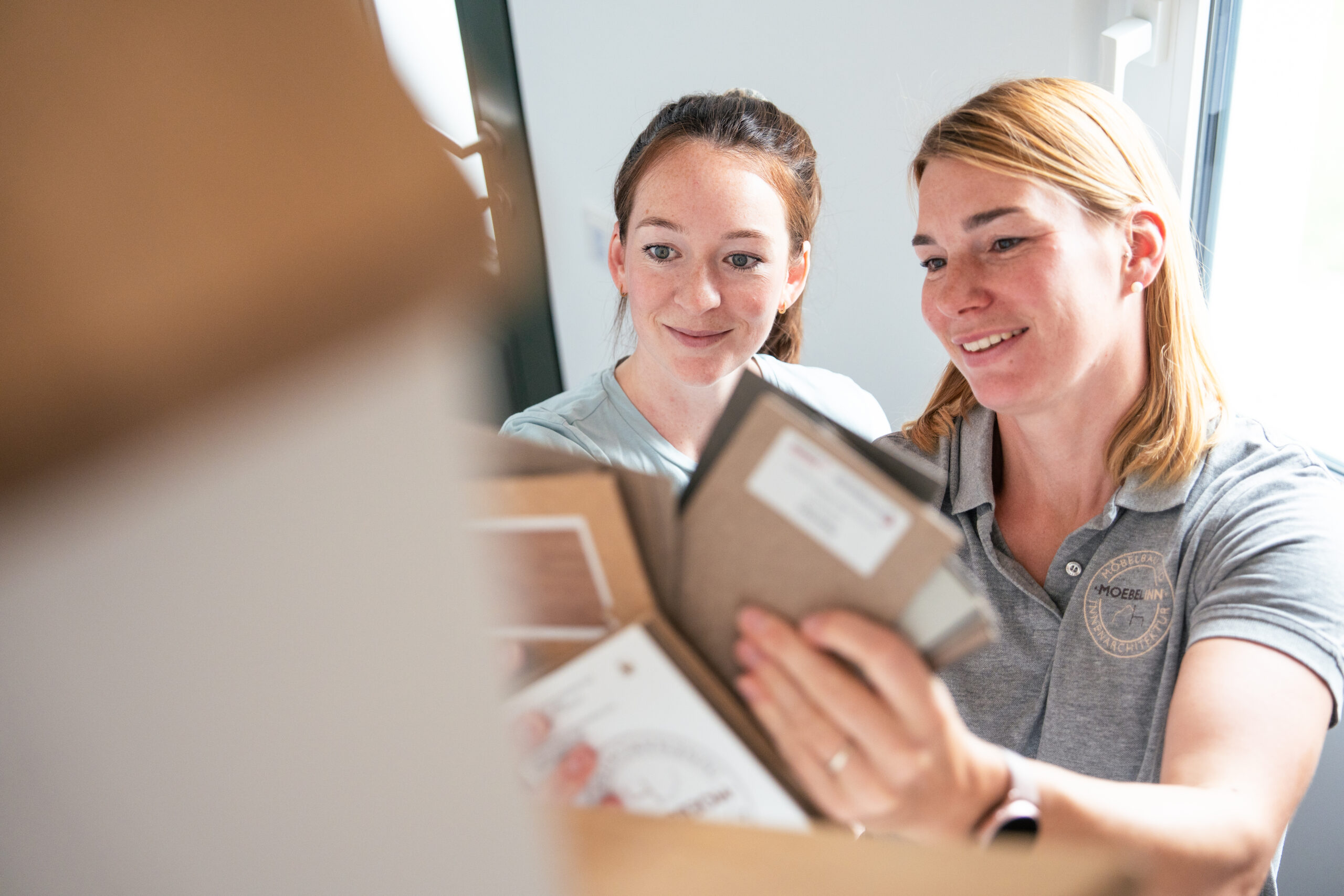 Zwei Frauen betrachten gemeinsam Material- und Farbmuster, lächelnd bei der Auswahl für ein Innenarchitekturprojekt.